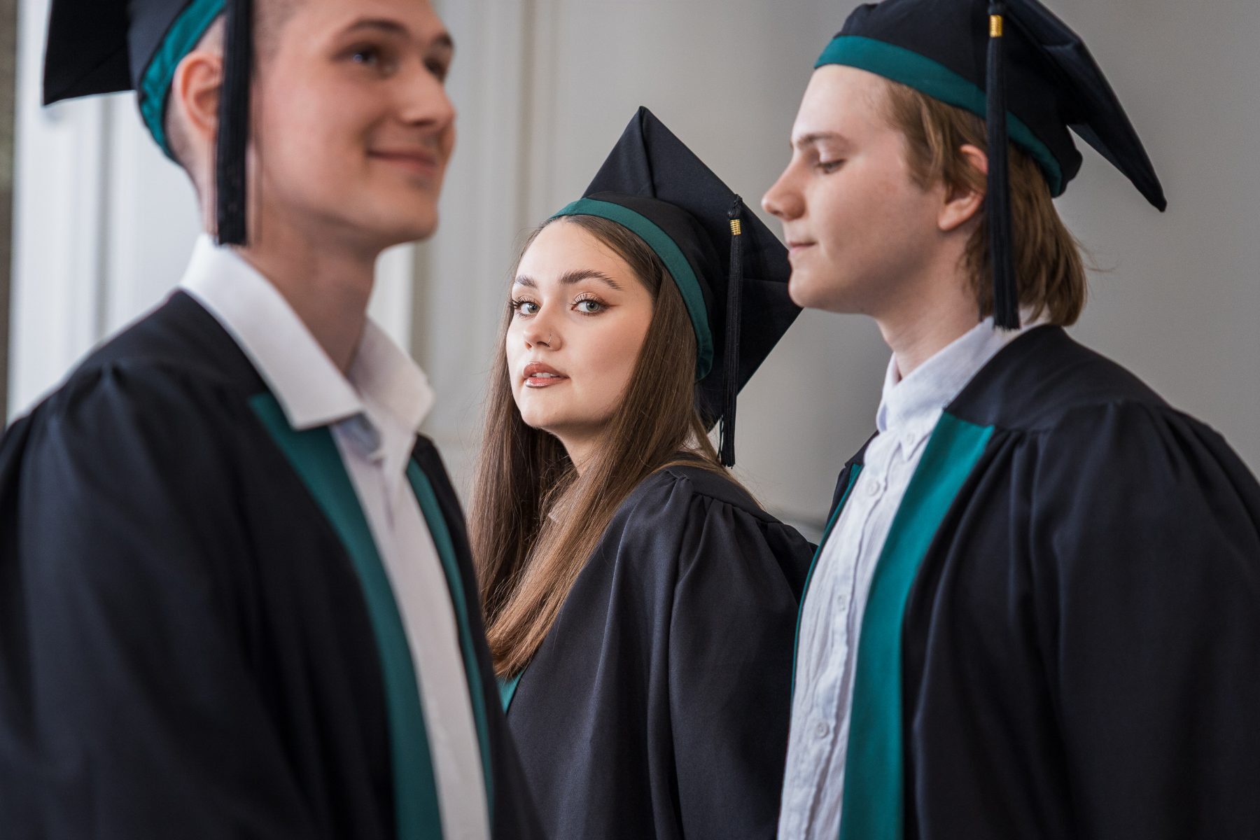 Three graduates in caps and gowns, the middle one turned to camera