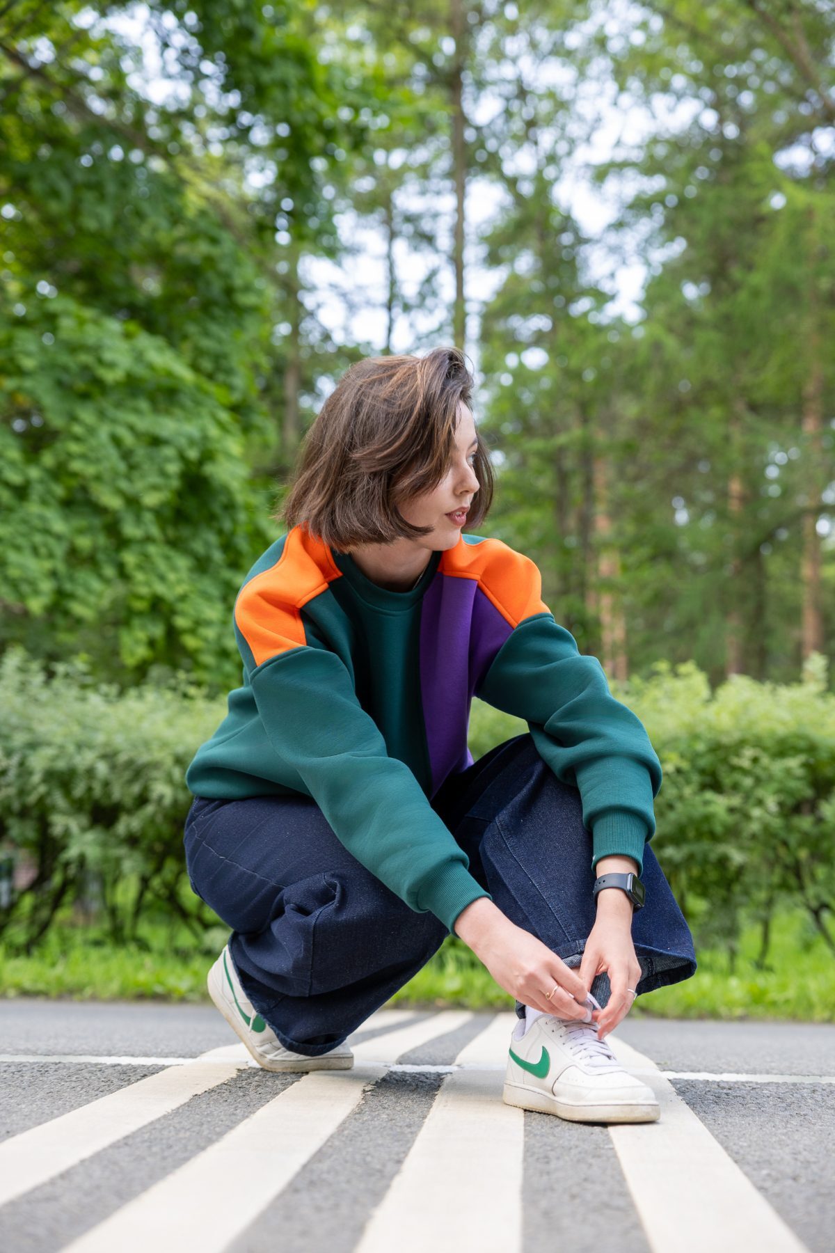 Model crouching on a crosswalk in a green, orange and purple colourblock sweatshirt