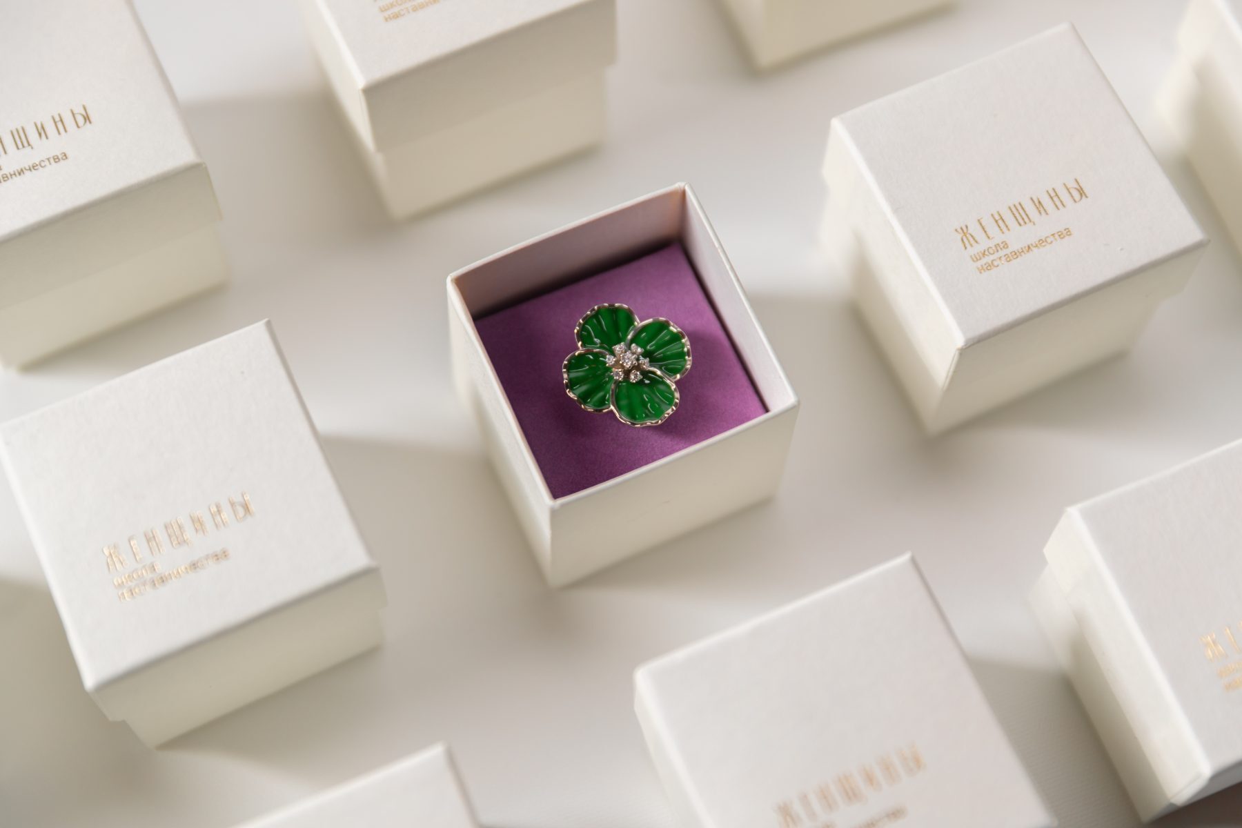 A green enamel flower pin in an open white gift box among closed boxes