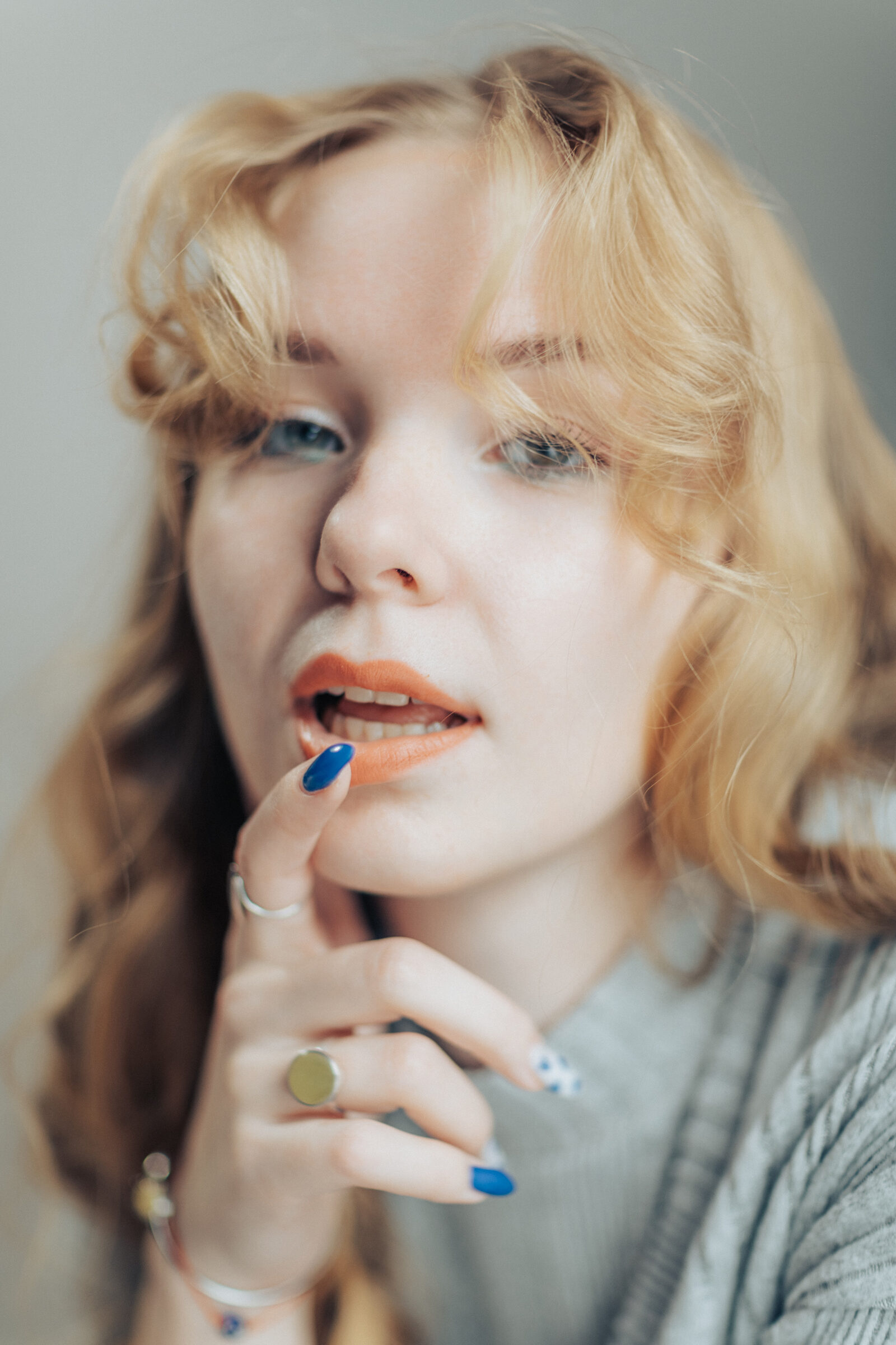 Soft close-up of a woman touching her orange lip with a blue-painted fingernail