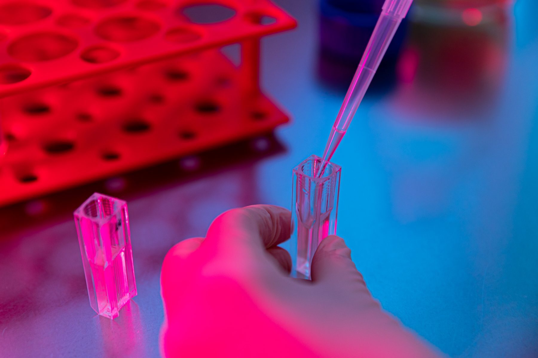 Researcher in safety glasses holding a small flask of red medium up to the light